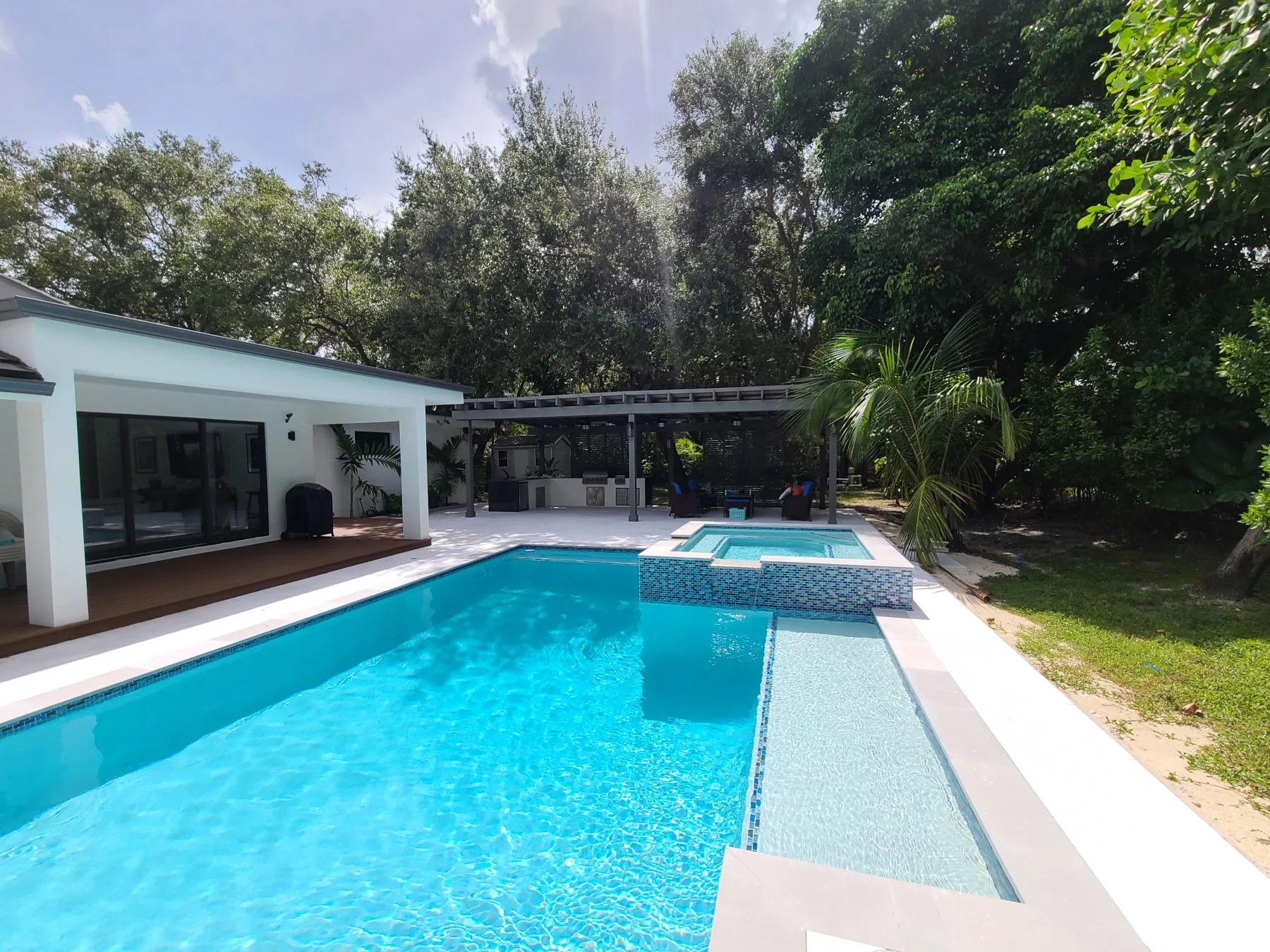 Full view of a modern pool and outdoor patio beside a white home