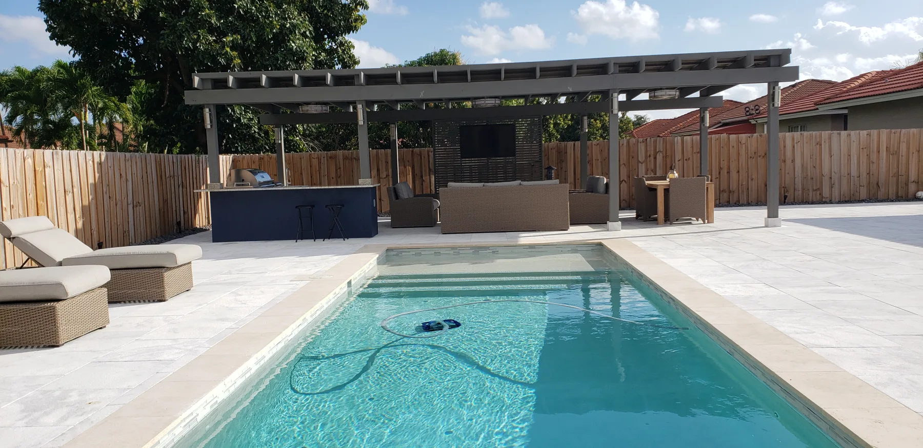 Pool and covered outdoor kitchen connected by a light stone patio