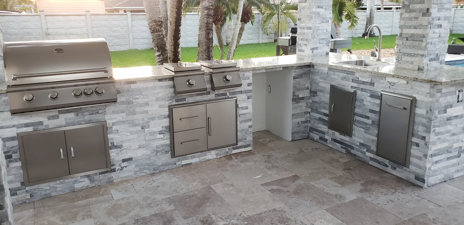 Built-in grill and stainless-steel appliances in a stone outdoor kitchen