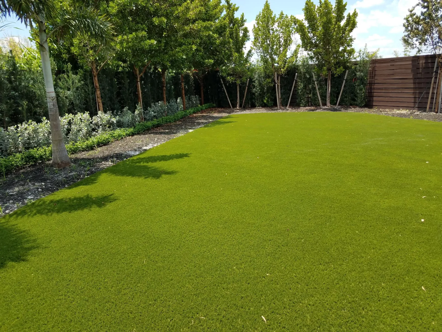 Wide synthetic turf lawn bordered by trees and planting