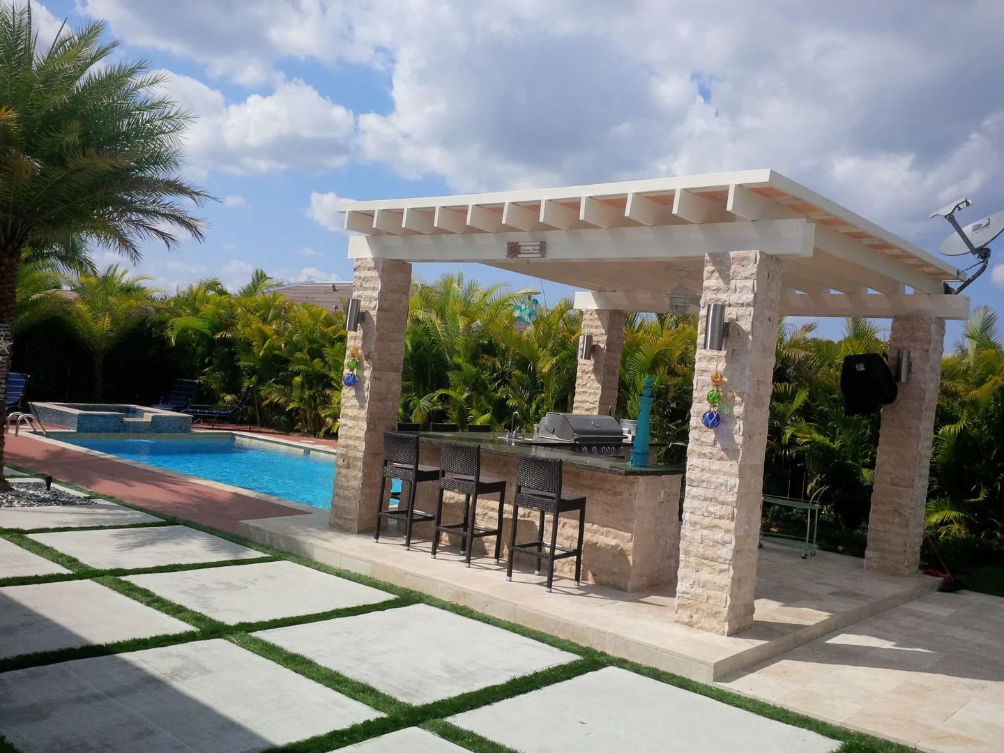 White pergola above an outdoor kitchen beside a swimming pool